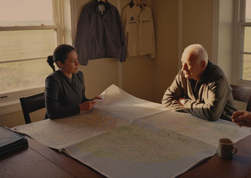 Two farmers reviewing paper field maps at a table in a Prairie farm office